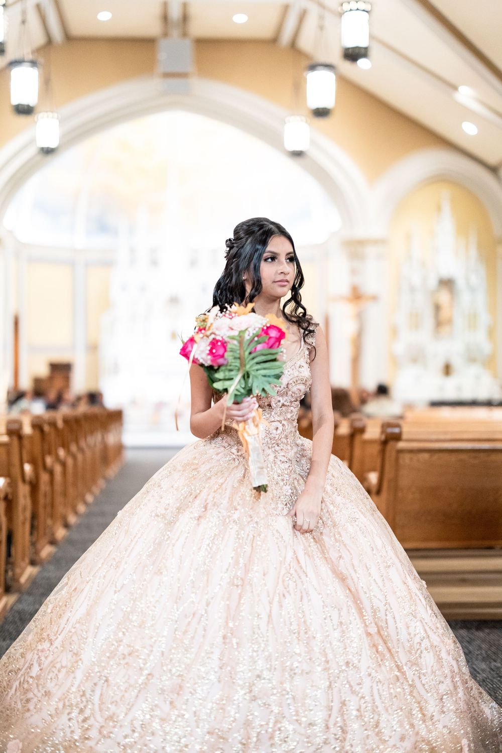 Quinceañera holding a floral bouquet inside a church.